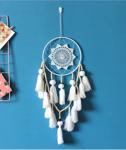 Handmade Nordic white dreamcatcher with tassels and wooden beads on a blue wall background.