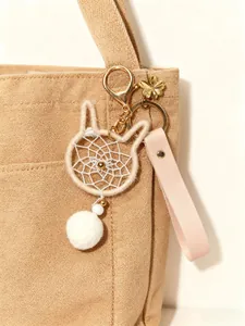 Close-up of a handmade cat-shaped dreamcatcher bag charm with a plush pom-pom.