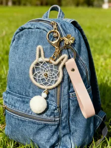 Close-up of handmade cat-shaped dreamcatcher keychain with plush pom-pom on denim bag