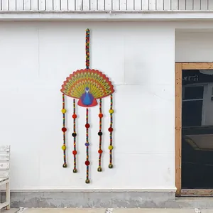 Scacciapensieri a forma di pavone in stile etnico con campanelli e pompon su muro bianco