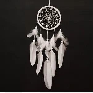 Détail d'un attrape-rêves blanc artisanal avec des plumes sur fond noir profond