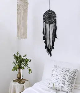 Handmade black dreamcatcher with feathers hanging on white wall in cozy bedroom.