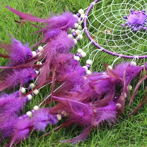 Detalle de un atrapasueños morado hecho a mano con plumas sobre hierba verde