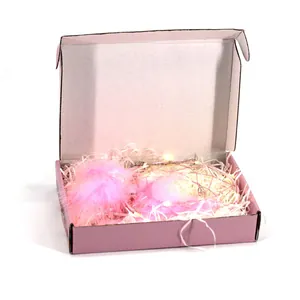 Detalle de una caja de regalo atrapasueños rosa con luces brillantes y papel triturado