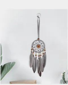 Retro handmade dream catcher with grey feathers hanging on a white wall