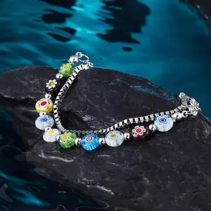 Detailansicht eines lebhaften zweilagigen Millefiori-Glasblumenarmbands auf Steinen.