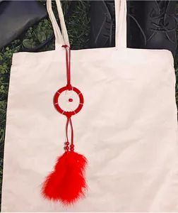Detalle de colgante atrapasueños rojo en un bolso de mano de lona color beige