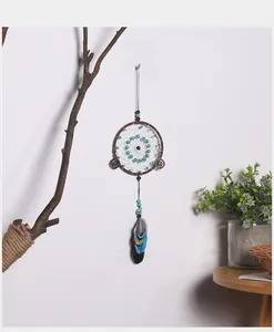 Atrapasueños vintage en una pared blanca junto a una rama rústica y una planta.