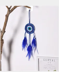 Détail d'un attrape-rêves bleu à l'œil maléfique avec plumes sur fond de mur blanc.