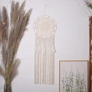 Handgemaakte bohemian dromenvanger met witte veren en kwastjes aan de witte muur.