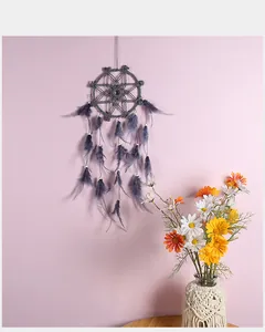 Atrapasueños boho gris hecho a mano con plumas suaves en una pared rosa pálido suave