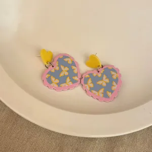 Close-up of heart-shaped acrylic earrings with pink scallop edges and yellow butterflies.