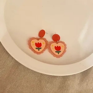 Close-up of heart-shaped acrylic earrings with red tulip pattern and wavy edges