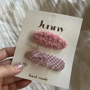Détail de barrettes à cheveux roses en peluche et en tweed sur une carte blanche.