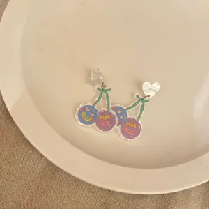 Close-up of cute quirky acrylic cherry earrings with smiley faces and heart studs