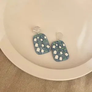 Close-up of quirky blue acrylic earrings featuring white lily of the valley design on a plate