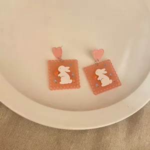 Close-up of cute acrylic biscuit-shaped earrings with rabbit and flower patterns