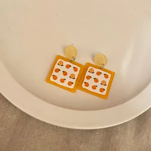 Close-up of quirky biscuit-shaped acrylic earrings with orange patterns on a plate