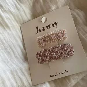Gros plan de barrettes en tweed rose avec paillettes et texture tissée sur carte.