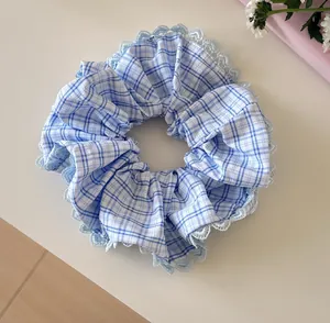 Detail shot of a blue plaid scrunchie featuring delicate light blue lace edge trim