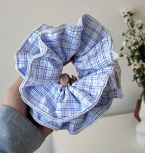 Detailed view of a large blue and white plaid fabric scrunchie hair tie held by hand
