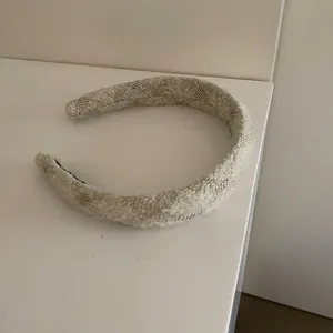 Dettaglio di un cerchietto intrecciato beige con sottili fili dorati scintillanti