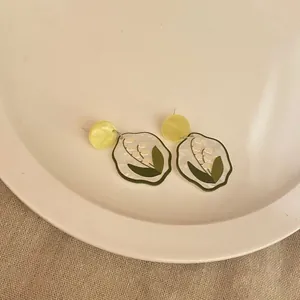 Close-up of cute acrylic earrings with white lily of the valley floral pattern detail.