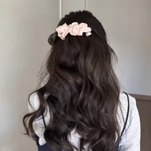 Back view of a woman wearing a soft pink pleated pearl hair clip on wavy hair