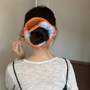 Back view of a stylish orange and blue zipper hair scrunchie holding a hair bun.
