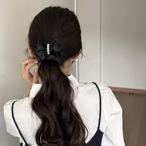 Elegant black satin bow hair clip with pearls shown worn on a wavy ponytail for a retro look