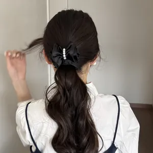 Elegant black satin bow hair clip with pearls securing a ponytail hairstyle detail view