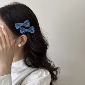 Detail showing a pair of blue denim bow hair clips worn on long dark wavy hair by a model.