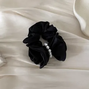 Elegant black satin hair scrunchie with white pearl detail on cream silk background