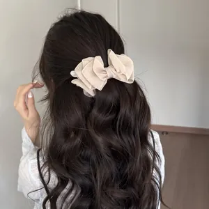 Vista posterior de un elegante clip de pelo con lazo de organza en cabello castaño ondulado