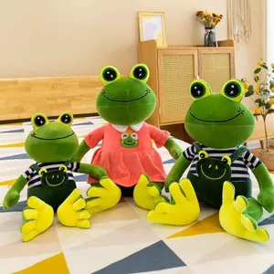 Cute green frog plush toys in pink dress and striped overalls sitting on a bed