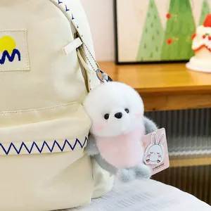 Close-up detail of a cute fluffy white and grey seal plush keychain hanging on a canvas bag