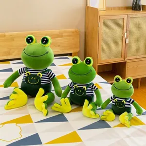 Three cute smiling frog plush toys in striped shirts and green overalls displayed on bed