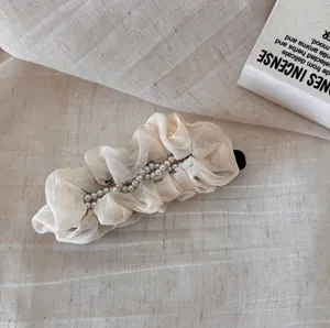 Detailed macro view of cream pleated chiffon banana clip with white pearl accents