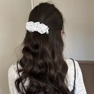 Elegant white ruffled pearl banana hair clip shown on wavy dark hair for a stylish look.