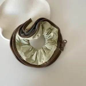 Detailed close-up showing the unique brown zipper trim on an olive green fabric scrunchie.