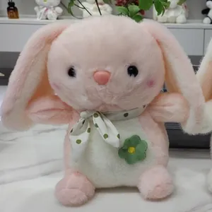 Detailed view of a soft pink plush rabbit wearing a green polka-dot scarf and flower.