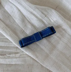 Detailed view of a blue denim bow hair clip with yellow stitching on white fabric