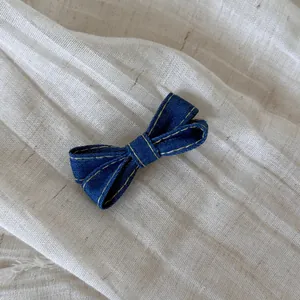 Detail view of a blue denim bow hair clip with yellow stitching on white fabric