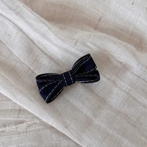 Close-up of a dark blue denim bow hair clip with yellow contrast stitching.