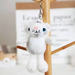Macro view of a soft white tiger plush keychain hanging on a minimalist wooden display stand.