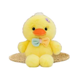Morbido peluche di anatra gialla con papillon colorato e accessorio caramella su bianco