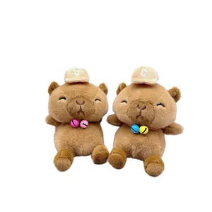Two cute brown capybara plush toys with hats and colorful bells on white background.