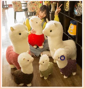 Diverse maten kleurrijke alpaca knuffels getoond met een glimlachende vrouw in een warme kamer