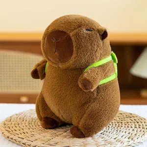 Adorable brown capybara plush toy with green harness accessory sitting on a rustic woven mat.