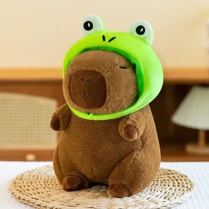Detail shot of a cute capybara plush toy wearing a bright green frog hat on a mat.